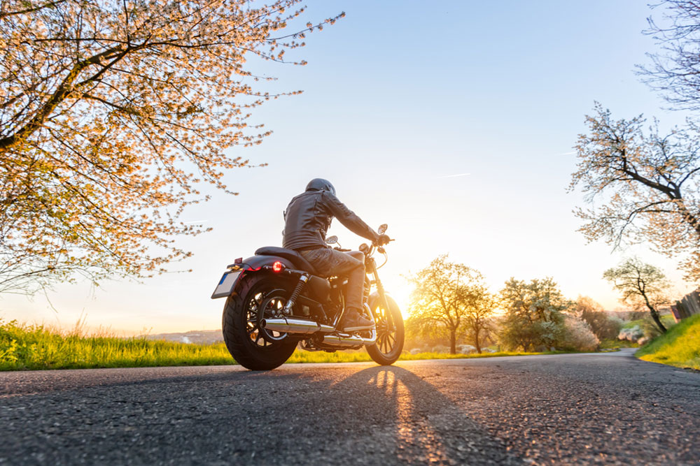 Young Motorcycle driver with helmet off stares toward sunrise